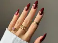 Main d'une femme aux ongles longs et pointus, vernis d'un profond couleur vernis automne. Bagues dorées ornées de pierres et de motifs.