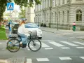 Kvinna på elcykel korsar övergångsställe. Trafik och byggnader i bakgrunden. Elcykel regler är viktiga för säkerheten.