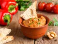 Un saporito pesto di peperoni in una ciotola di terracotta, accompagnato da crostini, noci e peperoni rossi freschi.