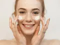Uśmiechnięta dziewczyna z piegami nakłada krem na twarz. Sudocrem na co? Na suchą skórę, podrażnienia, zaczerwienienia.