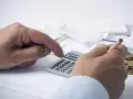Manos calculando con calculadora y lápiz, rodeado de recibos y monedas. ¿Qué significa grupo de cotización 10?