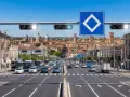 Traffico intenso in città con semaforo verde che indica via libera. Edifici storici sullo sfondo.