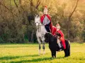 Zwei Reiter in römischer Kleidung, ein Erwachsener auf einem Schimmel und ein Kind auf einem Pony, reiten auf einer sonnigen Wiese. Ein fröhlicher Anblick, wie bei einem Martin Fest.