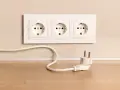Biały kabel z wtyczką leży na drewnianym blacie obok potrójnego gniazdka. Jak schować kable, by wyglądały estetycznie?