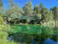 Puente verde cruza un río de aguas cristalinas y verdes, reflejando el bosque exuberante. Un lugar idílico para explorar el **alto tajo**.