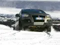 Un'auto con gomme invernali neve affronta un pendio innevato, sollevando spruzzi di bianco.