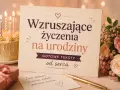 Urodzinowa kartka z napisem "Wzruszające życzenia na urodziny", obok tort z płonącymi świecami, prezent i bukiet róż. Idealna na wyjątkowe życzenia urodzinowe.