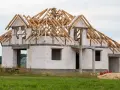 Dom w budowie z białych pustaków, z widoczną konstrukcją dachu. Zastanawiasz się, ile kosztuje pozwolenie na budowę?