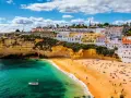 Coastal town with white buildings on cliffs overlooking a sandy beach and turquoise water.