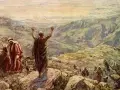 Balaam in the Bible, with arms raised, blesses Israel from a mountaintop. Another man in red looks on.