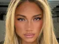 Primer plano de una mujer con cabello rubio y ojos separados, pecas sutiles y labios rosados.