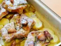 Pieczona karkówka z ziemniakami, czosnkiem i rozmarynem w naczyniu żaroodpornym.