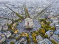 Pola Elizejskie z Łukiem Triumfalnym w Paryżu, otoczone kamienicami i drzewami w jesiennych barwach.