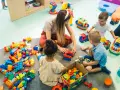 Dzieci bawią się klockami z opiekunką. Czy za żłobek się płaci? To pytanie zadają sobie rodzice, widząc radosne chwile swoich pociech.