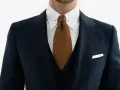 Elegancki mężczyzna w granatowym garniturze, białej koszuli i brązowym krawacie.