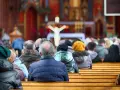 Ludzie siedzący w kościele, widok od tyłu, w tle ołtarz z krzyżem.