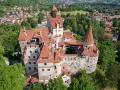 Dracula zamek, majestatyczna twierdza z czerwonymi dachami, otoczona zielenią i malowniczą wioską.