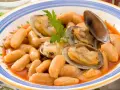 Plato de fabes con almejas, un guiso tradicional asturiano con judías blancas tiernas y jugosas almejas, decorado con perejil fresco.
