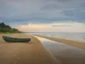 Zielona łódź na piaszczystej plaży Mierzei Wiślanej, idealne miejsce na camping. Woda odbija niebo, tworząc spokojny krajobraz.