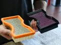 Hände halten zwei Luftfilter: einen orangen Standardfilter und einen schwarzen Sportluftfilter. Was bringt ein Sportluftfilter? Mehr Leistung!