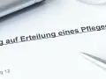 Ein Dokument mit der Überschrift "Antrag auf Erteilung eines Pflegegrads" liegt auf einem Tisch. Daneben liegen ein Stift und eine Brille.