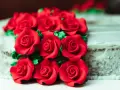 Un mazzo di rose rosse in pasta di zucchero adorna una torta.