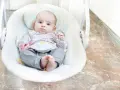 Uroczy niemowlak w bujaczku, z zaciekawieniem obserwuje otoczenie.