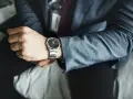 Mężczyzna w garniturze sprawdza czas na zegarku z metalową bransoletą. Może to być moment przed ważnym spotkaniem, wymagającym skracania bransolety w zegarku.