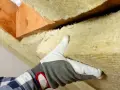 Ręka w rękawicy dociska wełnę mineralną do drewnianej konstrukcji dachu. To świetny materiał izolacyjny.