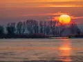 Zachód słońca nad zamarzniętym jeziorem. Piękna fotografia krajobrazowa z pomarańczowym niebem i sylwetkami drzew.