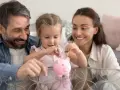 Rodzina z córką wrzuca monety do świnki-skarbonki. Planują przyszłość i świadczenia po urodzeniu dziecka.