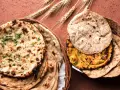 Dwa koszyki pełne pysznego chleba indyjskiego, w tym aromatyczny naan z kolendrą i klasyczny roti, ozdobione kłosami zboża.