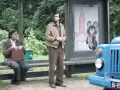 Deux hommes attendent à un arrêt de bus, un panneau des JO de Moscou 1980 avec Misha l'ours en arrière-plan. L'affaire Farewell se déroule.