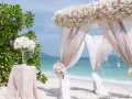 Romantyczny ślub na plaży. Biały baldachim ozdobiony różowymi i białymi kwiatami, zwiewne tkaniny i bukiety tworzą magiczną scenerię.