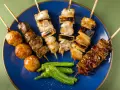 Różnorodne yakitori na niebieskim talerzu: kurczak, wątróbka, klopsiki i papryczki shishito.