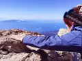 Blick vom Gipfel nach der Teide Wanderung. Ein Wanderer lehnt sich auf Felsen, mit Blick auf das weite Meer und ferne Inseln.