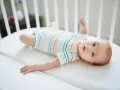 Niemowlę w kolorowym body leży w łóżeczku. Jego niebieskie oczy przypominają **perły Epsteina**, a uśmiech rozjaśnia pokój.