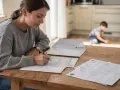 Frau füllt Formulare aus, während ihr Sohn spielt. Es geht um den kinderfreibetrag bei getrennten eltern.