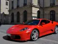 Czerwone Ferrari F430 zaparkowane na brukowanej ulicy przed kamienną kamienicą.