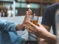 Dłoń odrzuca szklankę z alkoholem. Przykład asertywnego odmawiania picia alkoholu.