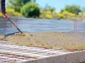Coulée de béton frais sur une armature métallique pour assurer l'épaisseur dalle maison. Le travailleur étale le béton avec une pelle.