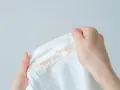 Dłonie trzymają białą koszulę z plamami po fluidzie. Jak sprać fluid? Podpowiedź na zdjęciu.