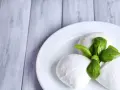 Trzy kulki serka mozzarella z listkami bazylii na białym talerzu. Idealne do sałatki, znasz ser mozzarella kcal?