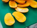 Pokrojone w łódeczki, soczyste mango w intensywnym kolorze, jakby w ciąży z owocową obfitością, leżą na zielonej desce.