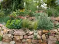 Ein wunderschöner Steingarten, der zeigt, wie man mit wenig Geld einen tollen Garten gestalten kann. Bunte Blumen und Gräser wachsen zwischen Natursteinen.