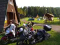 Motocykliści odpoczywają na kempingu w Rumunii, otoczeni drewnianymi domkami i lasem.