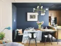 El azul oscuro combina con tonos pastel, madera y dorado. Un comedor elegante con mesa, sillas negras, lámpara dorada y flores.
