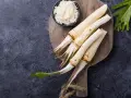 Frische Meerrettichwurzeln und geriebener Meerrettich auf einem Holzbrett. Manche Frauen fragen sich, ob Meerrettich in der Schwangerschaft erlaubt ist.