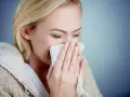 Kobieta z blond włosami chusteczką wyciera nos, cierpiąc na objawy alergii na pyłki.