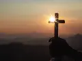 Dłoń trzyma krzyż na tle zachodzącego słońca. Promienie przebijają przez krzyż, symbolizując nadzieję i zasady Wielkiego Postu.